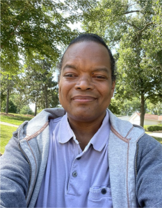 A man in a blue shirt and jacket smiling for the camera.