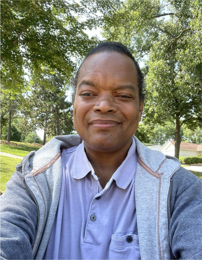 A man in a blue shirt and jacket smiling for the camera.